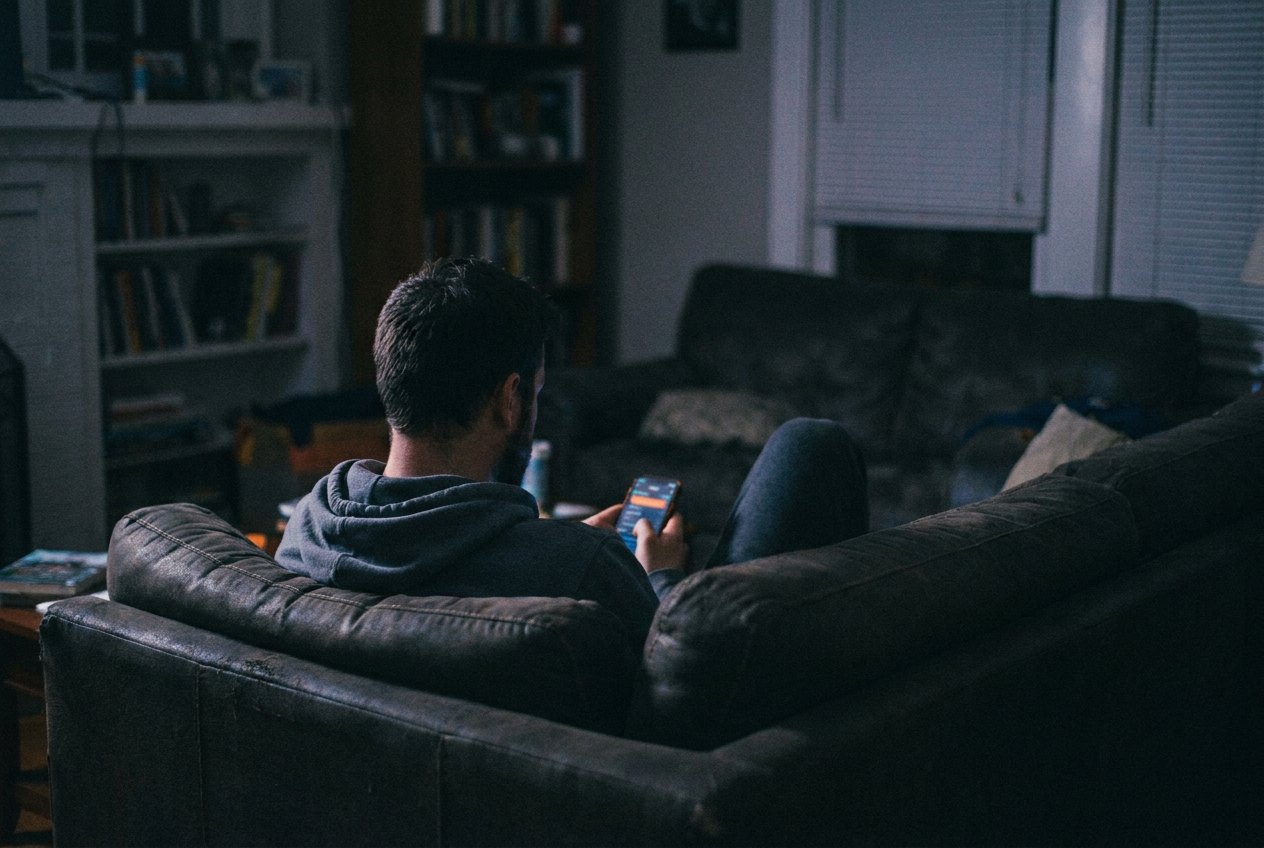 A man sitting alone in a dark room at night, lit by his phone.